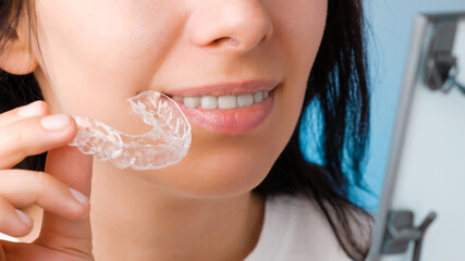 Close up woman holding a transparent removable braces for perfect smile and looking to the mirror. Orthodontic aligners for straightening and whitening teeth.