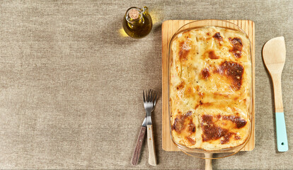 Freshly baked hot lasagna with melted cheese and gratin served with a wooden spatula and made with olive oil on a rustic table with copy space
