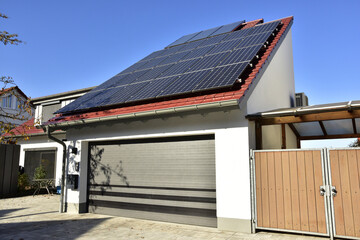 Garage mit Automatik-Rolltor und Pult-Ziegeldach mit grossflächiger Photovoltaikanlage, angebaut an ein modernes Einfamilienhaus - obrazy, fototapety, plakaty