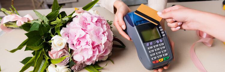 Cropped view of customer paying with credit card by terminal in hands of florist near fresh bouquet on desk, banner