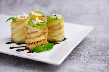 Zucchini appetizer rolls with cream cheese and basil on white plate on gray background. Fried vegetable marrow sushi rolls. Fried zucchini.