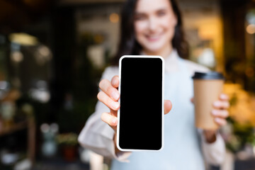 young florist holding smartphone with blank screen and coffee to go on blurred background