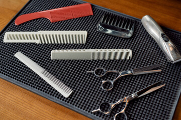 Fototapeta premium Professional barber tool kit. Scissors, combs for hair and beard, hair clipper are lying on a rubber mat in the barber shop