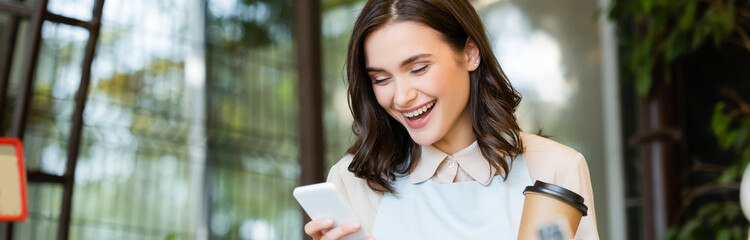 cheerful florist holding coffee to go and messaging on smartphone during brake, banner