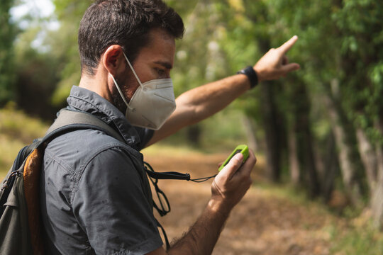 Man looking at the GPS pointing out the direction of the right route while hiking in the mountain with a mask on the covid-19. Concept of sport. Nature and environment