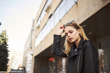 Woman model in a black jacket near a tall building on the street 