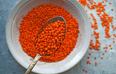 Red lentils in a plate. Vintage spoon and plate on a gray background.