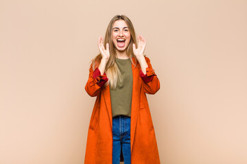 blonde woman feeling shocked and excited, laughing, amazed and happy because of an unexpected...