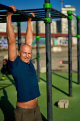 Photo of muscular man doing pull ups on horizontal gymnastic bar during morning workout by seaside