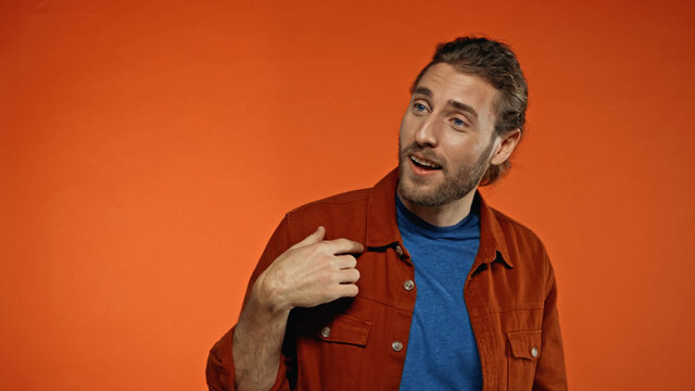 flattered young and bearded man smiling on orange