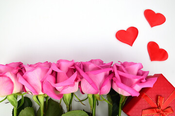Fototapeta na wymiar Roses are arranged in a row next to a red gift box and three decorative hearts.