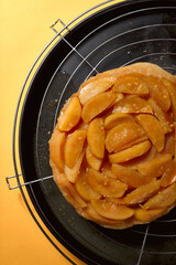 Top Shot von frisch gebackener Apfel Tarte Tatin auf Kuchengitter mit gelbem Hintergrund