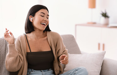 Asian woman listening to music in headphones and dancing