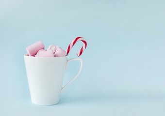 pink marshmallow in white cup with candy canes on blue background. Christmas card concept