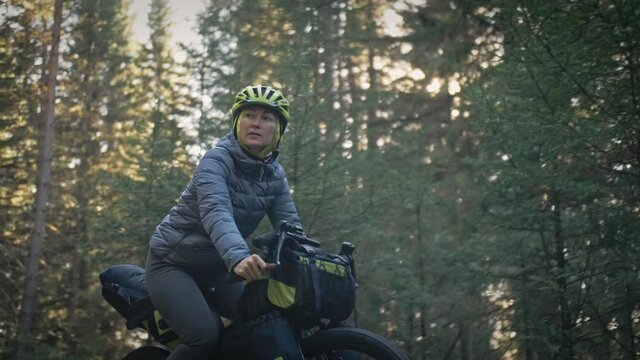 The woman travel on mixed terrain cycle touring with bike bikepacking outdoor. The traveler journey with bicycle bags. Stylish bikepacking, bike, sportswear in green black colors. Magic forest park.