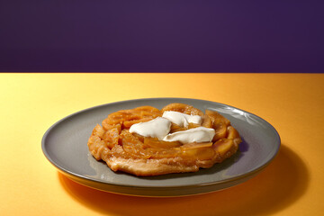 Apfel Tarte Tatin mit Créme Fraiche auf grauem Teller mit gelbem und lila Hintergrund