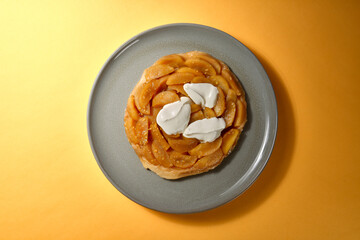 Top Shot von Apfel Tarte Tatin mit Créme Fraiche auf grauem Teller mit gelbem Hintergrund