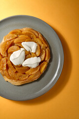 Top Shot von Apfel Tarte Tatin mit Créme Fraiche auf grauem Teller mit gelbem Hintergrund