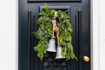 Christmas wreath with bells on entrance vintage black door outside. Veranda front door decorated by...