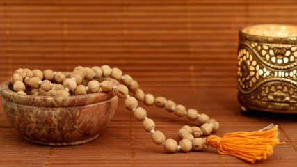 Bowl with mala beads and golden candle on wooden background with copy space. Essential accessory...