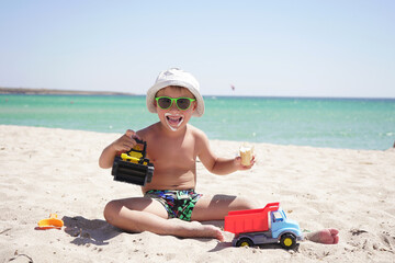 Happy child in a Panama hat and sunglasses on a sandy beach and eating ice cream. Azure sea on a Sunny summer day on the horizon.