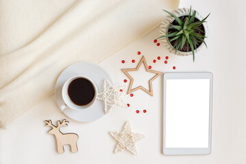 A digital tablet with a blank screen, lies on a white table surrounded by flat wooden Christmas decorations