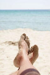 close-up of a man's legs lying on the seashore, azure sea on the horizon.