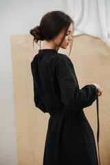 Mannered young beautiful woman tying her dress on a waist. Hair in a bun, head half-turned, in profile. From behind.