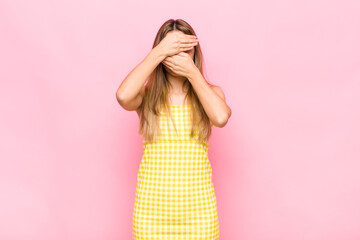 blonde woman covering face with both hands saying no to the camera! refusing pictures or forbidding...
