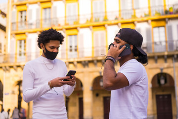 Black Latino friends talking on the phone with face mask. Friendships in the coronavirus pandemic, covid-19. Social distance, new normal