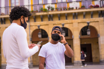 Black Latino friends talking on the phone with face mask. Friendships in the coronavirus pandemic, covid-19. Social distance, new normal