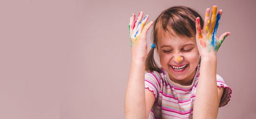 Beautiful young happy girl with children's face makeup and painting colorful hands. Free space for...