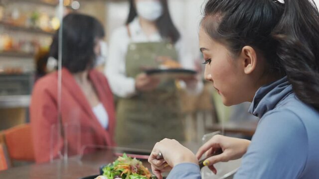 Asian female eating salad and waitress serving food to another woman.