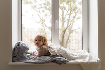 Child lying on the window in living room and watching at the street. cozy home on weekends, holidays and lockdown