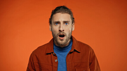 shocked young man with open mouth looking at camera on orange