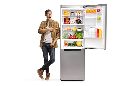 Full length portrait of a young man pointing at a fridge with food