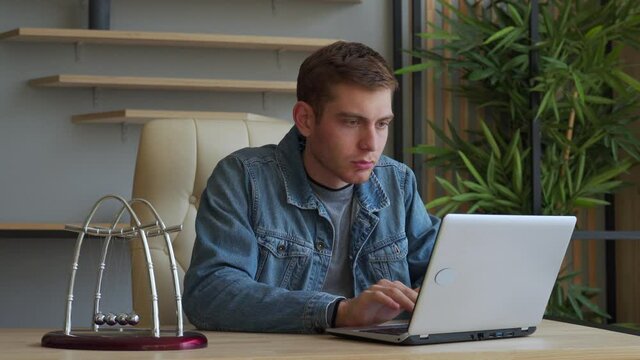 A business person looks at the computer screen in the office. Tired businessman playing with kinetic balls