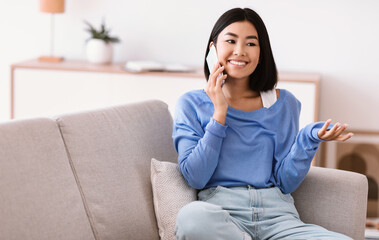 Smiling asian woman talking on cellphone sitting on couch