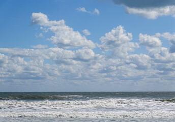 Fototapeta na wymiar Beautiful white puffy cloudscape over a rough ocean with wild waves