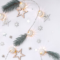 Christmas composition of wooden stars, a garland of white luminous balls, fir branches, bells and snowflakes on a white background.