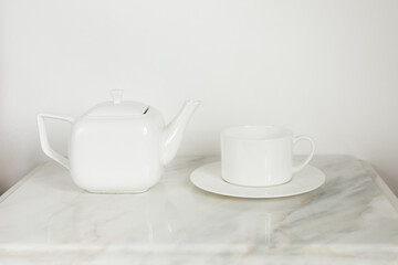 Fototapeta na wymiar white ceramic tea pot and white tea cup on a white plate on marble coffee table 