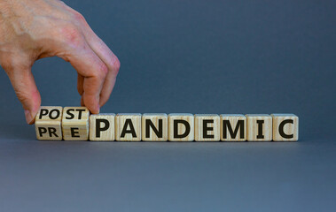 Symbol for a post-pandemic time. Male hand turns cubes and changes the words 'pre-pandemic' to 'post-pandemic'. Beautiful grey background. Medical and covid-19 post-pandemic concept, copy space.