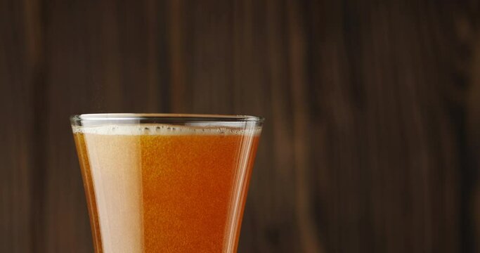Cold beer is slowly poured into a glass on a dark wooden background, there is a lot of foam and bubbles in the glass. Slow motion. Beer is pouring into a glass isolated on a wooden background. 