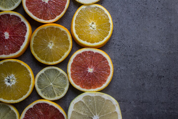 Naklejka na ściany i meble Fruit frame or border. Fresh juicy orange, lemon and grapefruit slices on a table. Dark gray background with copy space. Healthy eating concept. 