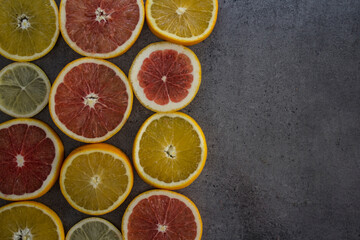 Fototapeta na wymiar Fruit frame or border. Fresh juicy orange, lemon and grapefruit slices on a table. Dark gray background with copy space. Healthy eating concept. 