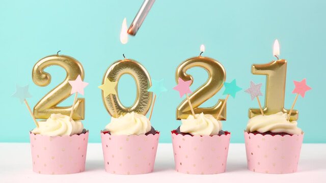 2021 Happy New Year's Eve pastel pink and blue theme cupcakes with large gold candles. Lighitn candles.