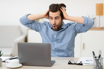 Shocked Frustrated Businessman Looking At Laptop Touching Head At Workplace