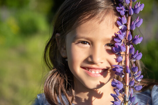Closeup face of a beautiful little girl with a lupin flower. Happy childhood