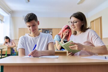 Lesson in class of high school students, female teacher sitting at desk with student