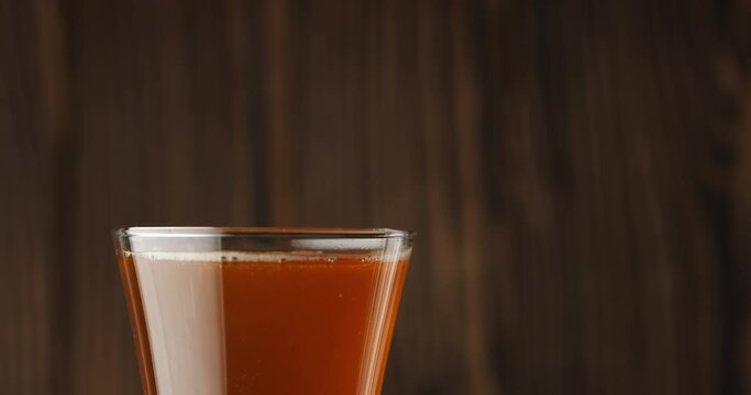 Cold beer is slowly poured into a glass on a dark wooden background, there is a lot of foam and bubbles in the glass. Slow motion. Beer is pouring into a glass isolated on a wooden background. 